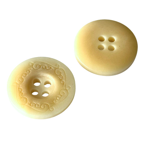 Knopf in Creme-Gelb, Vorderseite mit Ornamentrand um vier Loecher, Rueckseite glatt mattgelb
