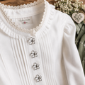 Silberfarbener Blumenknopf auf weißer Trachtenbluse mit Spitzenbesatz – dekorativer Ösenknopf für Dirndl, Trachtenmode und elegante Nähprojekte.