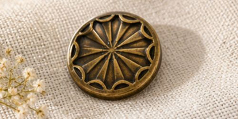 Knopf bronzefarben mit strahlenfoermigem Sternmuster und geperlter Randverzierung, auf Leinenstoff